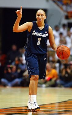 a women who is holding a basketball in her hand and walking on the court with other people watching