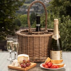 a wicker picnic basket with cheese, bread and wine on a patio table next to a bottle of champagne