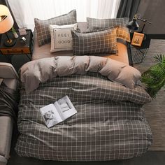 a bed with grey and brown comforter next to a lamp on a table in front of a window