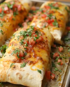 several burritos with tomatoes and cheese on a baking sheet