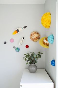 a white shelf topped with a vase filled with flowers next to space related wall hangings