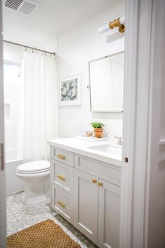 a bathroom with white cabinets and gold hardware on the vanity, along with a beige rug