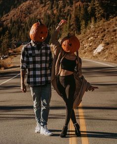 a man and woman wearing pumpkin heads walking down the road with their arms in the air