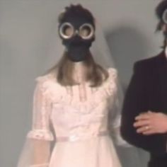 a man and woman wearing gas masks standing next to each other in front of a wall