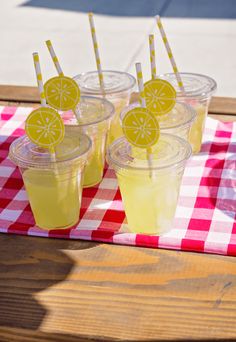 four cups with lemonade and straws on a checkered tablecloth