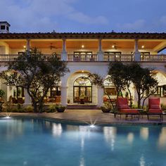 a large house with a pool in front of it at night, surrounded by trees and lawn furniture