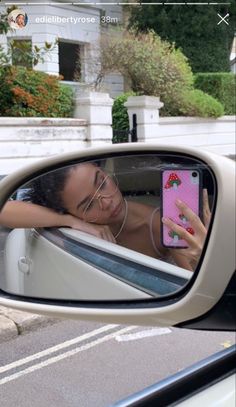 a woman taking a selfie in the side mirror of a car with her cell phone