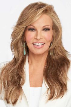 a woman with long hair wearing a white blazer and green earrings smiling at the camera