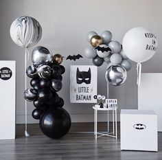 an assortment of black and white balloons in a room with batman decorations on the wall