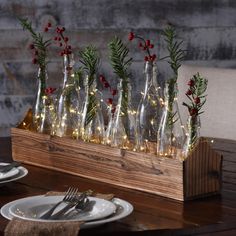 a wooden table topped with lots of glass bottles filled with christmas lights and greenery