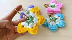 three crocheted flowers are being held up by someone's hand on a table