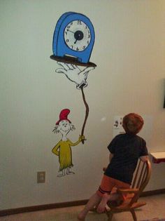 a child sitting in a chair looking at a clock painted on the wall