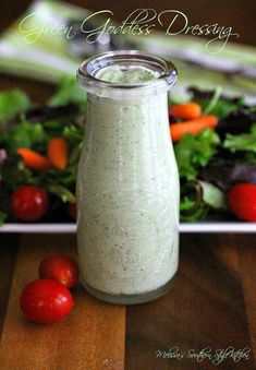 a salad dressing in a glass jar on a table with tomatoes and lettuce