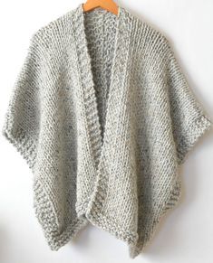 a knitted sweater hanging on a hanger next to a white wall with a wooden hanger