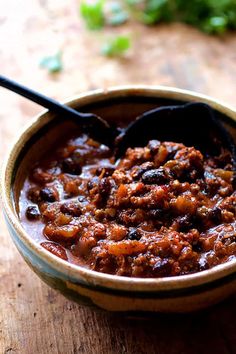 a bowl filled with chili sitting on top of a wooden table next to a spoon