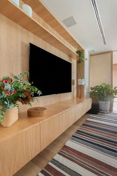 a flat screen tv sitting on top of a wooden shelf next to potted plants