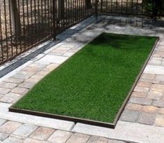 artificial grass is laid out in the middle of a brick walkway and fenced area