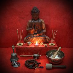 a buddha statue sitting on top of a red table next to candles and other items