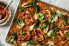 a pan filled with noodles and tofu next to a bowl of sauce on the side