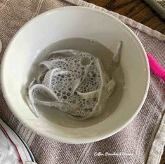 a white bowl filled with liquid next to a pink toothbrush on top of a table