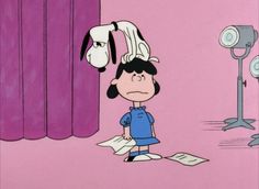 a charlie brown cartoon character standing in front of a purple curtain with a dog on his head