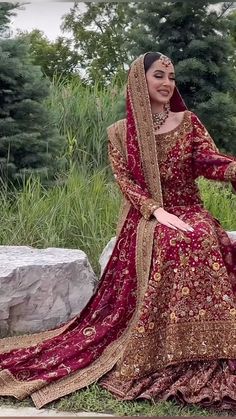 a woman in a red and gold bridal gown sitting on a rock with her arms outstretched