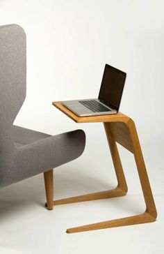 a laptop computer sitting on top of a wooden table next to a gray chair with legs