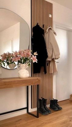 a room with a mirror, coat rack and flowers on the table in front of it