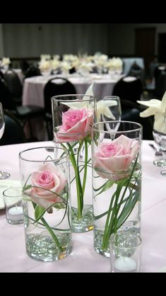 three vases filled with pink roses sitting on top of a white table cloth covered table