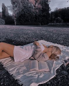 a woman laying on top of a blanket reading a book