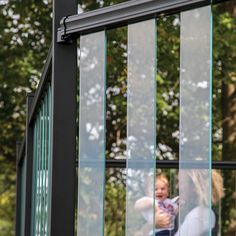 a woman holding a baby in her arms while looking out the window at trees and grass