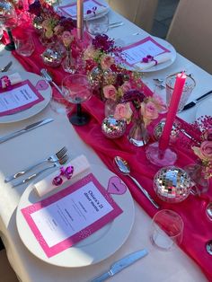 the table is set with pink and silver place settings, plates, napkins, utensils