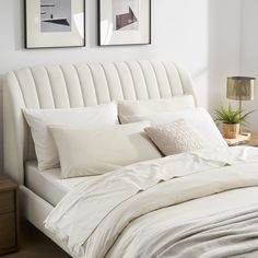 a bed with white sheets and pillows in a bedroom next to two pictures on the wall