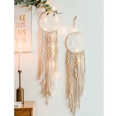 two white dream catchers hanging on the wall with string lights and greenery next to them