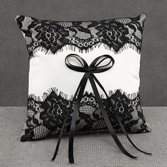 a black and white lace pillow with a bow on the front is sitting on a gray surface