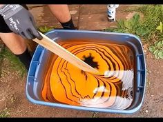 a person is painting an orange in a blue container with a wooden spatula on it