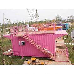 a pink building with stairs and tables on the ground next to it in an open field