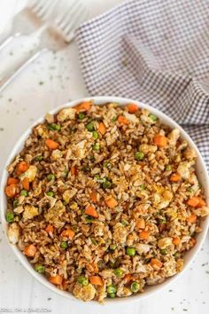 a bowl filled with rice and vegetables on top of a white tablecloth next to a fork