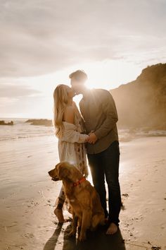 a man and woman standing next to a dog on the beach