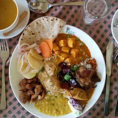 a white plate topped with meat and veggies next to two cups of coffee