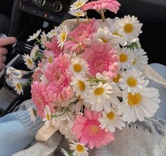 a bouquet of pink and white daisies in someone's lap with their hand on the steering wheel