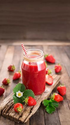 strawberry juice in a jar with strawberries scattered around it on a wooden table top