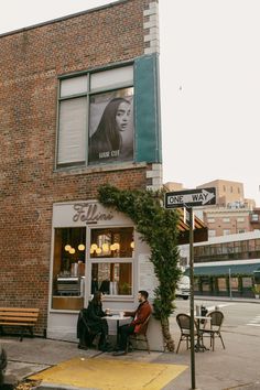 two people sitting at a table in front of a building with an advertisement on it