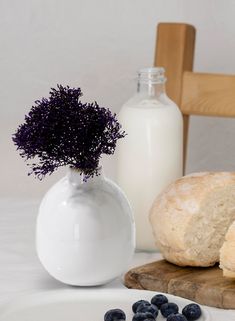 a white vase filled with blueberries next to a loaf of bread and a bottle of milk