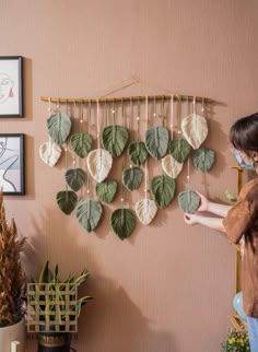 a woman standing in front of a wall hanging with leaves