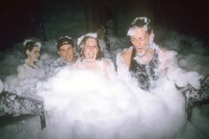 four people in bathtub with foam all over their faces and body, surrounded by bubbles