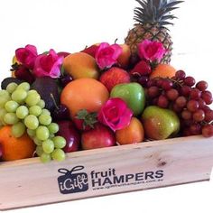 a wooden crate filled with assorted fruit including grapes, oranges and pineapple