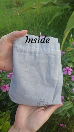 someone holding up a small pouch with the word inside on it in front of some flowers