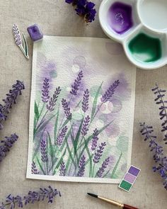 some purple flowers are sitting on a table next to watercolor paints and paintbrushes