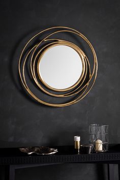 a round mirror hanging on the wall above a console table with candles and vases